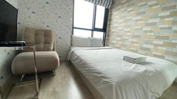 A hotel room with a bed, a chair, a television, and a window with a striped curtain.