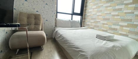 A hotel room with a bed, a chair, a television, and a window with a striped curtain.