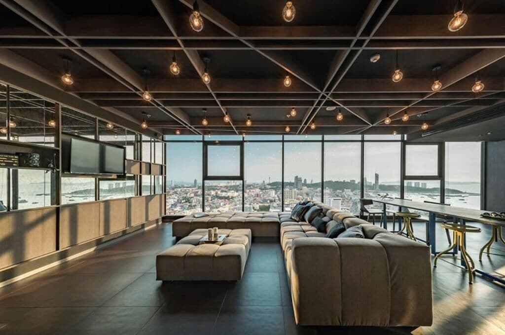 A modern lounge area with a large sofa, a coffee table, and a dining table with chairs. There is a large window offering a view of a cityscape.