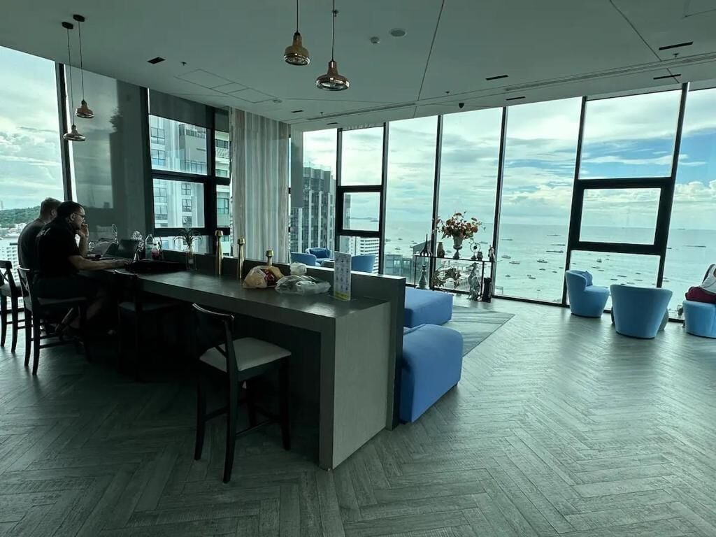 Un intérieur moderne avec un îlot de cuisine, un coin salon et de grandes fenêtres offrant une vue sur la mer.