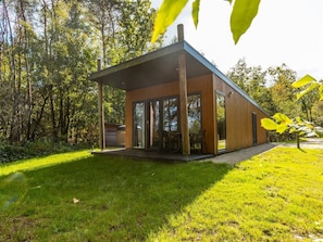 A modern wooden cabin with large windows, a covered patio, and a surrounding forest. - De Wiltzangh - Bosrand Wellness Cabin | 2p by Interhome (Ruinen)