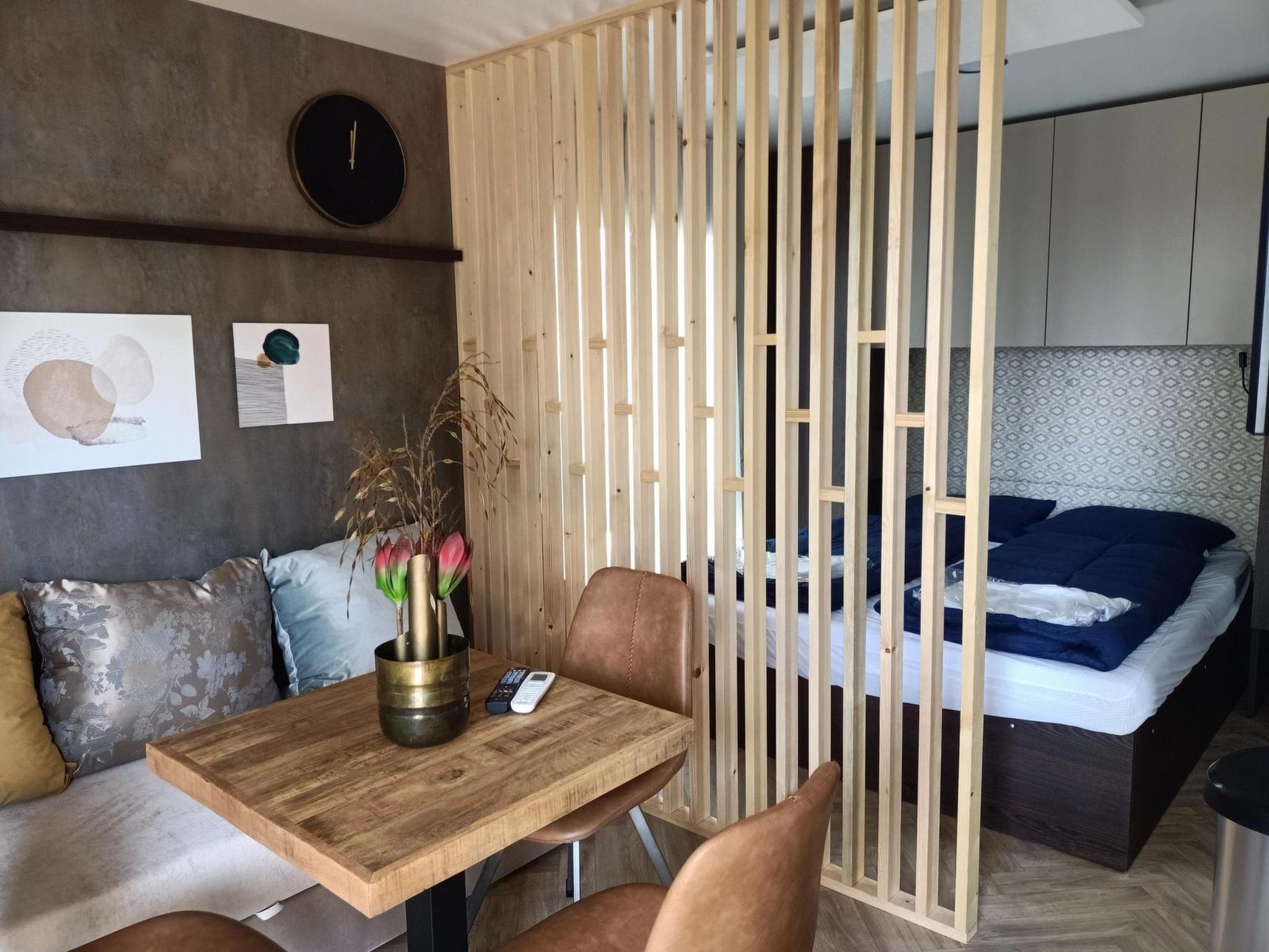 Un dormitorio moderno con cama, un separador de madera, un escritorio con un florero y un sofá.