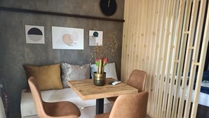 A modern living space with a wooden table, two chairs, a sofa with cushions, and a decorative vase with flowers.