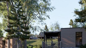 A modern cabin with a deck overlooking a pond, surrounded by trees and a grassy area.