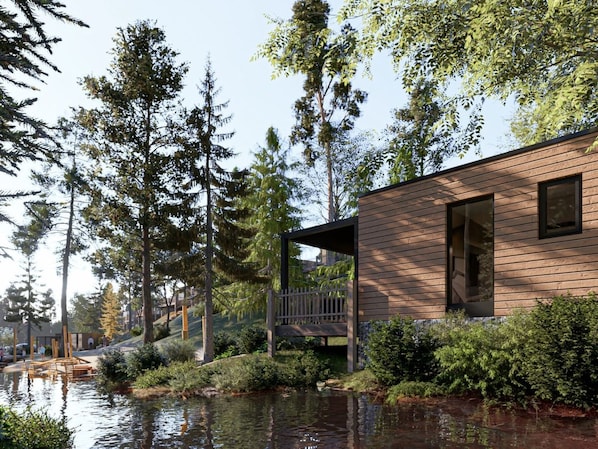 A modern wooden cabin with a deck overlooking a body of water, surrounded by trees.