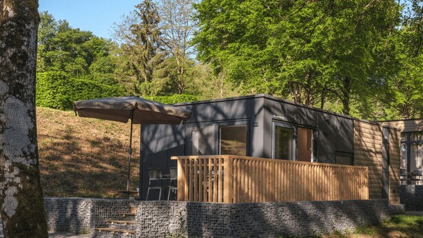 A modern cabin with a deck, surrounded by trees and a stone wall. - Resort Walsdorf - Moezel Lodge by Interhome (Luxembourg)