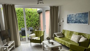 A modern living room with a green sofa, white armchairs, a coffee table, and a TV on a stand. - Bungalowpark Herkingen - Casa Ina by Interhome (Herkingen)