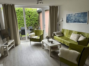 A modern living room with a green sofa, white armchairs, a coffee table, and a TV on a stand. - Bungalowpark Herkingen - Casa Ina by Interhome (Herkingen)
