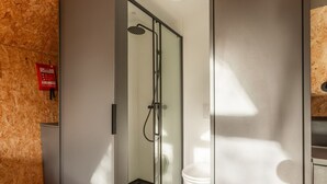 A modern bathroom with a glass shower enclosure, a toilet, and a visible fire extinguisher.