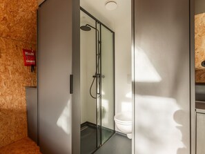 A modern bathroom with a glass shower enclosure, a toilet, and a visible fire extinguisher.