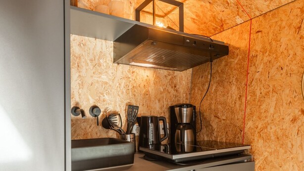 A compact kitchen with a stainless steel sink, a coffee maker, and a range hood.