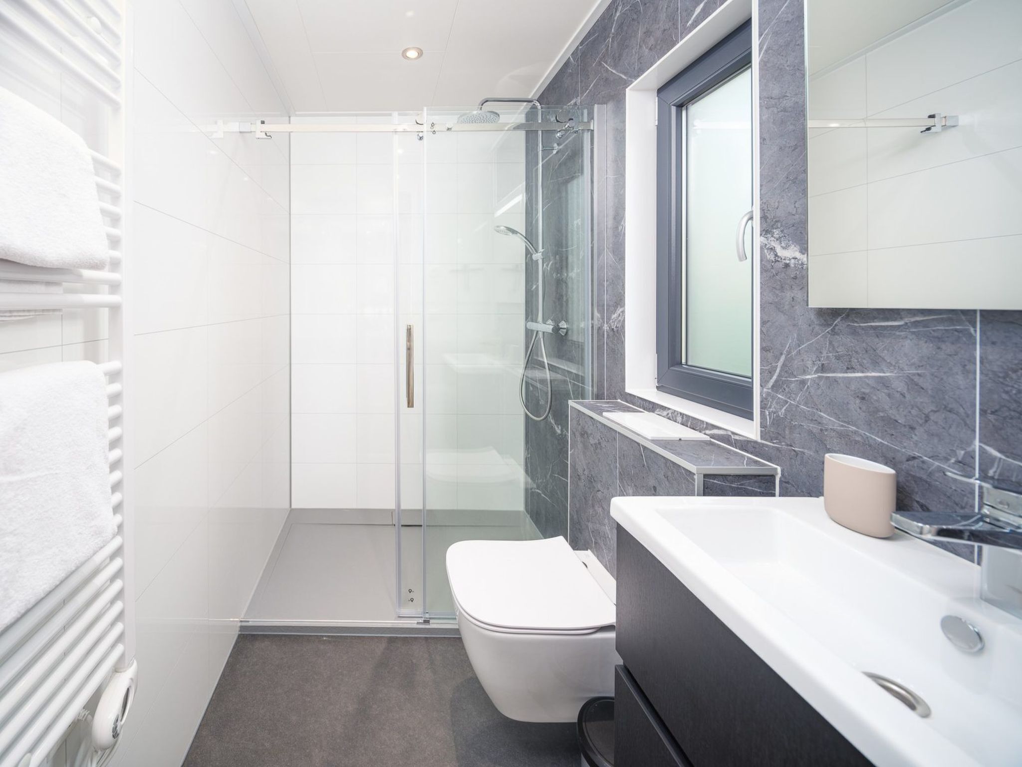 Une salle de bain moderne avec une douche à parois de verre, des toilettes et un meuble-lavabo avec un miroir.