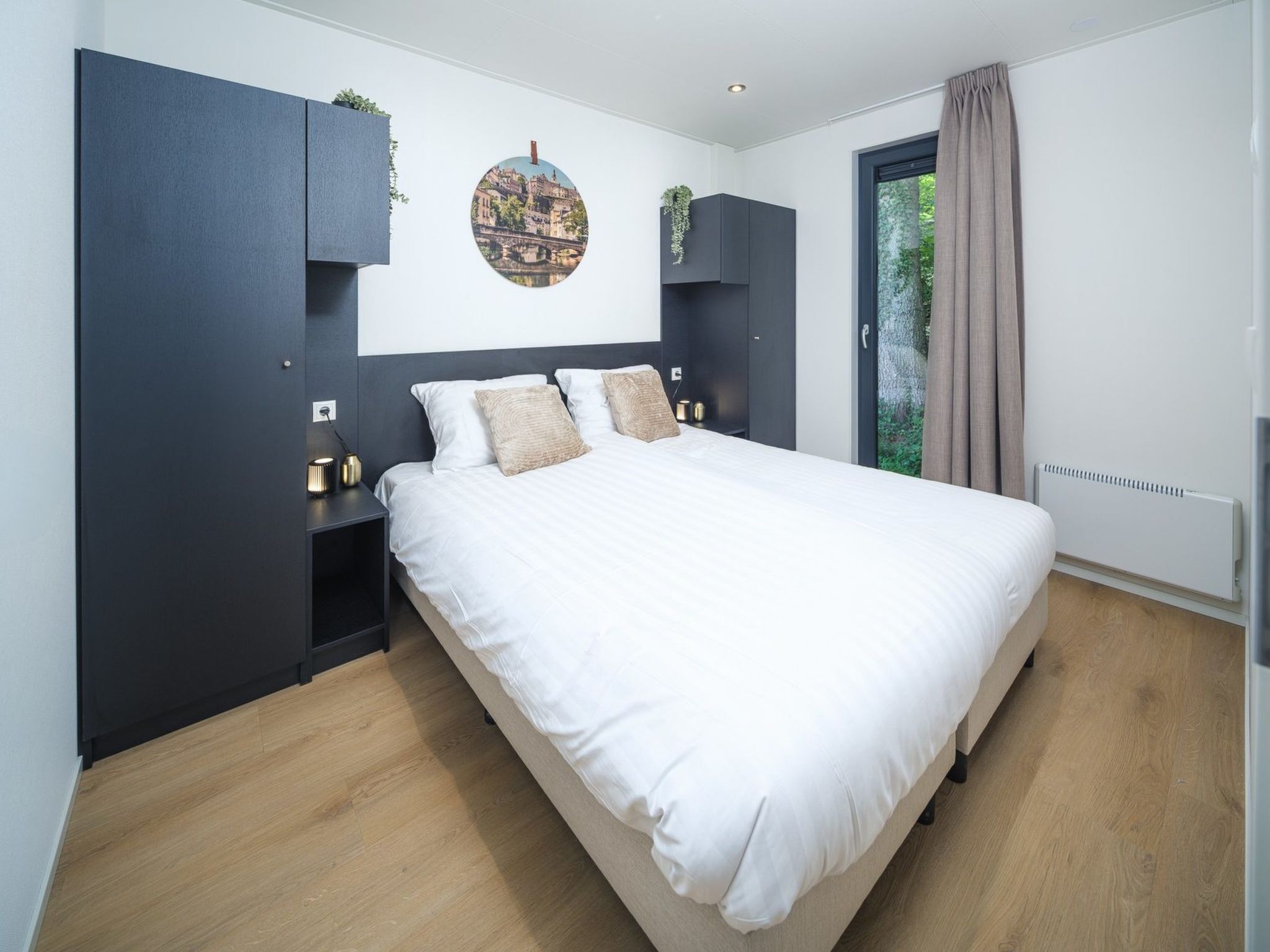 Een moderne slaapkamer met een groot bed, donkere kasten, een aan de muur bevestigd schilderij en een raam met gordijnen.