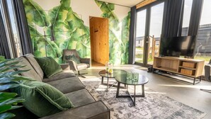 A modern living room with a large window, a sofa, a coffee table, and a TV. - Vakantiepark Aan de Maas - Weide Lande | 4p by Interhome (Kerkdriel)
