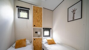 A bedroom with two beds, a wooden cabinet, a window, and a giraffe picture on the wall. - Vakantiepark Aan de Maas - Weide Lande | 4p by Interhome (Kerkdriel)