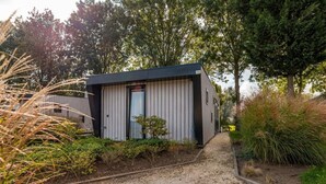 A modern, single-story building with a dark roof and light siding, surrounded by gravel paths and greenery. - Vakantiepark Aan de Maas - Weide Lande | 4p by Interhome (Kerkdriel)