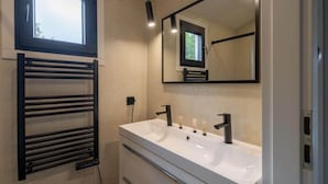 A modern bathroom with a large window, a built-in towel rack, a sink with two faucets, and a mirror above the sink. - Wilsumer Berge Resort - Nature Lodge Hottub by Interhome (Wilsum)