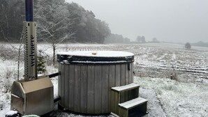 A cylindrical water heater with a wooden structure beside it, set in a snowy field with trees in the background. - Wilsumer Berge Resort - Nature Lodge Hottub by Interhome (Wilsum)