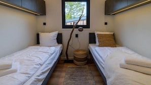 A small, modern room with two single beds, a window with a view of trees, and a decorative branch hanging from the ceiling. - Wilsumer Berge Resort - Nature Lodge Hottub by Interhome (Wilsum)