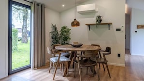 A dining area with a round wooden table, six chairs, a hanging pendant light, and a plant on a shelf. - Wilsumer Berge Resort - Nature Lodge Hottub by Interhome (Wilsum)