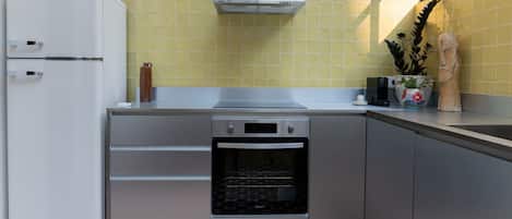 Una cocina compacta con horno integrado, extractor de acero inoxidable y refrigerador blanco.