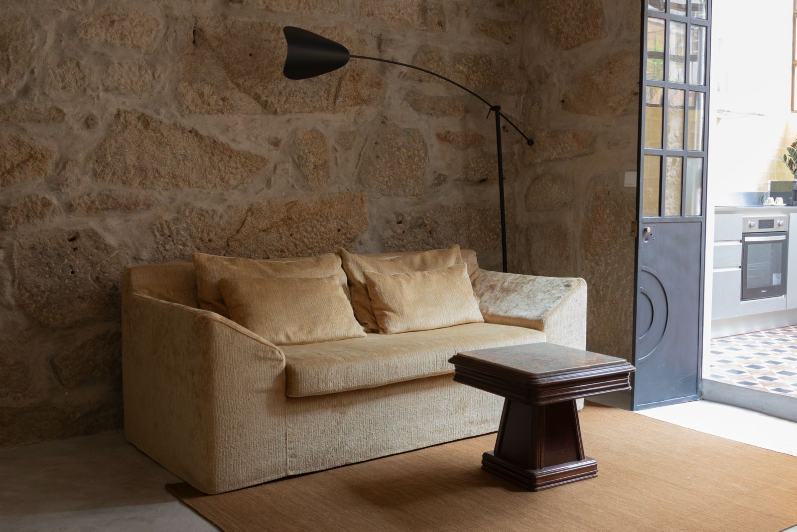 A room with a stone wall, a beige sofa, a wooden coffee table, and a black floor lamp.