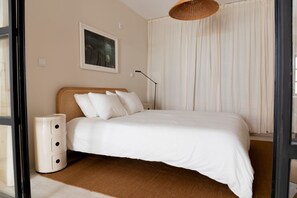 A bedroom with a bed, a bedside lamp, a wall-mounted picture, and a window with curtains. - Private Atrium Guest Suite in Porto (Porto)