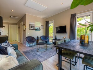 Ein modernes Wohnzimmer mit einer Couch, Sesseln, einem Esstisch und einem Fernseher.
