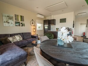 Ein modernes Wohnzimmer mit einer Eckcouch, einem runden Esstisch und einer Küche im Hintergrund.