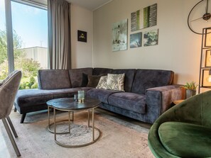 Ein modernes Wohnzimmer mit einem Ecksofa, einem runden Couchtisch und einem grünen Sessel.