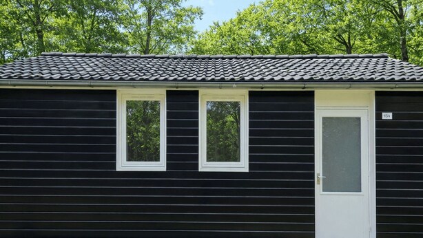 A black building with two windows and a door, surrounded by a grassy area and trees. - De Wiltzangh - Boschborg Lodge | 4p by Interhome (Ruinen)