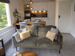 A modern living room with a grey sofa, a wooden coffee table, and a view of a kitchen with pendant lighting. - De Wiltzangh - Boschborg Lodge | 4p by Interhome (Ruinen)