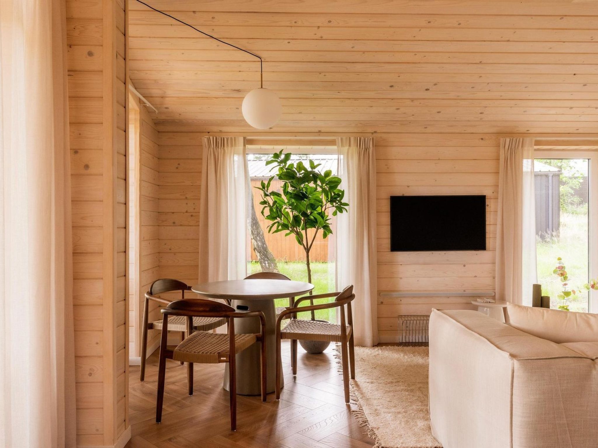 Een houten interieur met een eettafel, stoelen, een bank, een televisie en een plant.