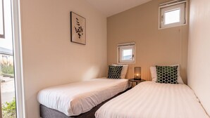 A bedroom with two beds, a bedside table with a lamp, a window, and a wall-mounted picture. - Vakantiepark Aan de Maas - Weide Lande | 6p by Interhome (Kerkdriel)