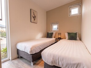 A bedroom with two beds, a bedside table with a lamp, a window, and a wall-mounted picture. - Vakantiepark Aan de Maas - Weide Lande | 6p by Interhome (Kerkdriel)