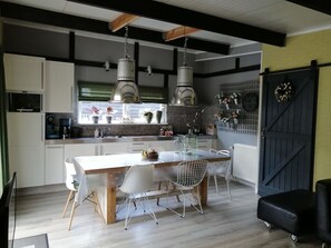 Eine moderne Küche mit Essbereich, ausgestattet mit einer großen Kochinsel, Pendelleuchten und einer Ziegelrückwand.