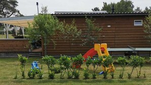 A playground with slides and climbing structures, surrounded by small trees and a building in the background. - Wilsumer Berge Resort - Green Forest by Interhome (Wilsum)