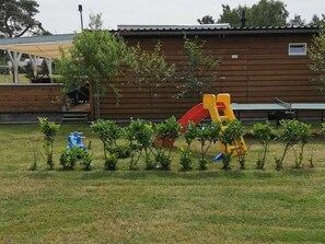 Ein Spielplatz mit Rutschen und Klettergerüsten, umgeben von kleinen Bäumen und einem Gebäude im Hintergrund.