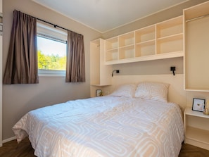 Ein Schlafzimmer mit einem großen Bett, Einbauschränken, einem Fenster mit Vorhängen und einem Nachttisch mit Bilderrahmen.