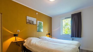 Una camera da letto con un letto, comodini, una lampada, una finestra con tende e due quadri appesi al muro.