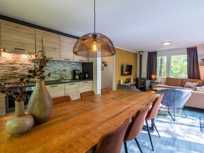 Eine moderne Küche mit Steinrückwand, ein Essbereich mit Holztisch und Stühlen sowie ein Wohnzimmer mit Sofa und Kamin.