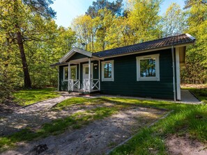 Eine eingeschossige Holzhütte mit Veranda, umgeben von Bäumen.