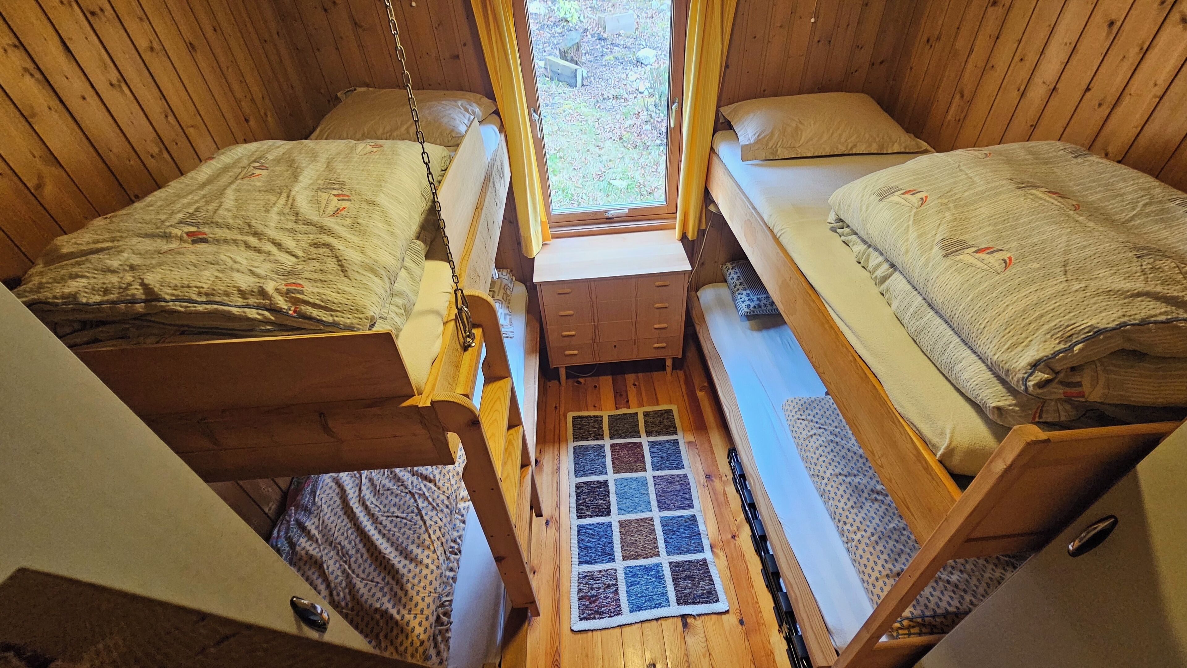 A compact room with two bunk beds, a small wooden dresser, and a window with a view of the outdoors.