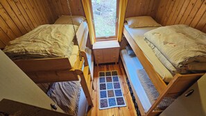 Een compacte kamer met twee stapelbedden, een klein houten dressoir en een raam met uitzicht op de omgeving.