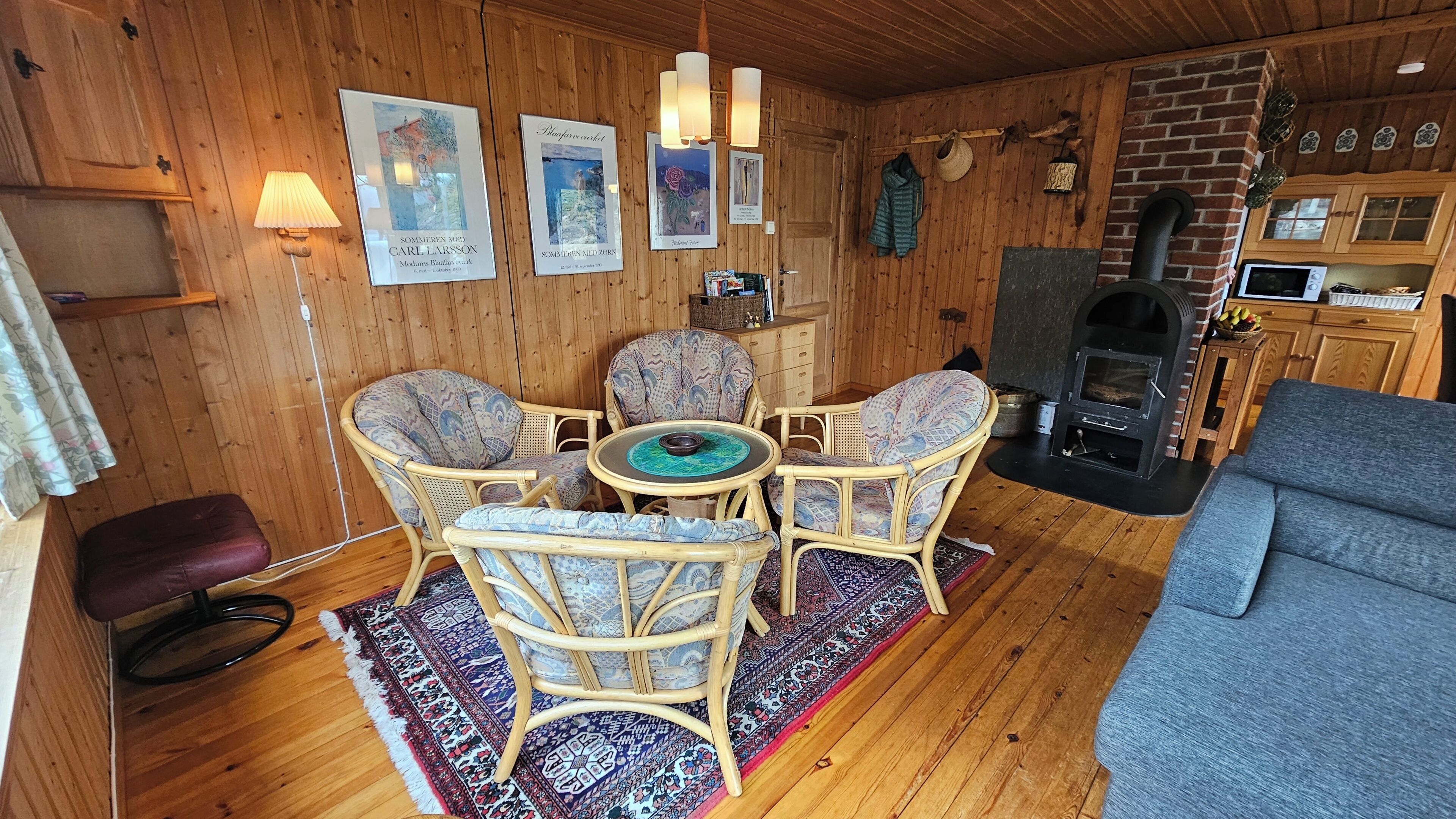 A cozy room with a wooden interior, a fireplace, a dining area with wicker chairs, and a sofa.
