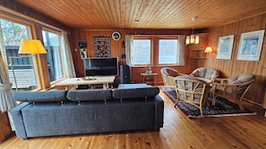 A cozy cabin interior with a sofa, a table, a television, and a fireplace.