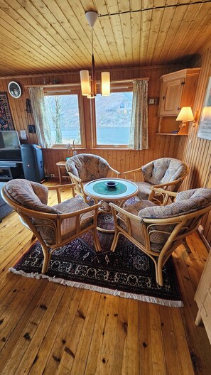 Un cuarto acogedor con techo de madera, una mesa redonda con sillas, una alfombra y vistas al exterior a través de ventanas.