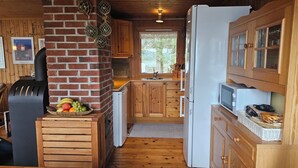 A compact kitchen with wooden cabinets, a brick wall, a window, and a refrigerator.