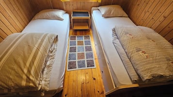 A small, cozy room with two beds, a small table, and a rug.