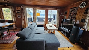 Een gezellige woonkamer met een grijze bank, een houten salontafel, een televisie en een groot raam met uitzicht op de omgeving.